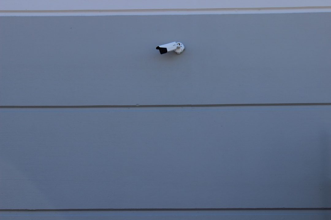 White bullet security camera mounted on the gray exterior wall of a warehouse